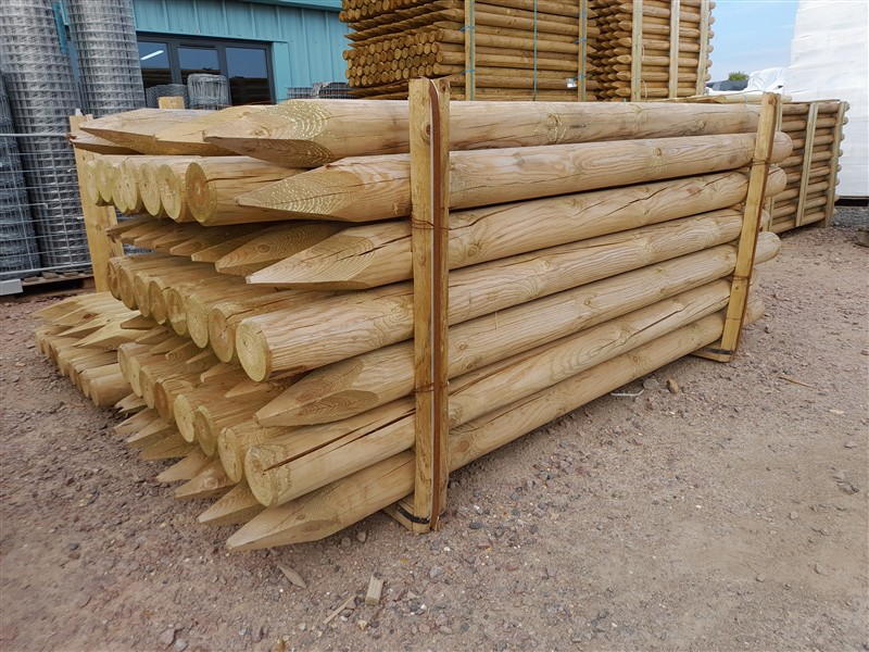 Stacked pointed wooden fence posts in yard