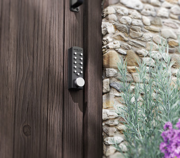 Modern keypad door lock beside stone wall and lavender
